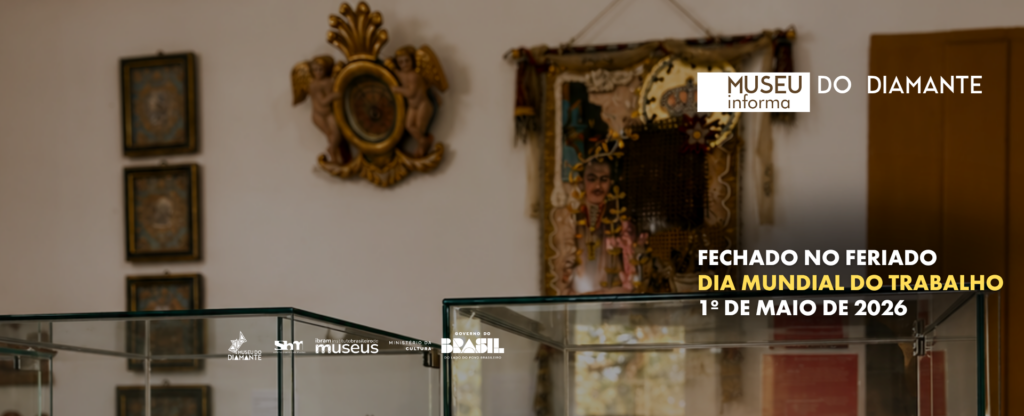 Fotografia com texto sobreposto. Card informativo institucional do Museu do Diamante. A imagem mostra o interior de uma sala expositiva, com vitrines de vidro. Ao fundo, há objetos decorativos e obras religiosas penduradas na parede. Sobre a fotografia, lê‑se: “Museu do Diamante informa”. Em destaque, o aviso: “Fechado no feriado – Dia Mundial do Trabalho – 1º de maio de 2026”. No rodapé do card aparecem as logomarcas do Museu do Diamante, do Sistema Brasileiro de Museus, do Instituto Brasileiro de Museus, do Ministério da Cultura e do Governo Federal do Brasil.